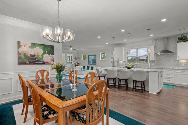 dining area featuring light wood-style flooring, ceiling fan with notable chandelier, a wainscoted wall, recessed lighting, and ornamental molding