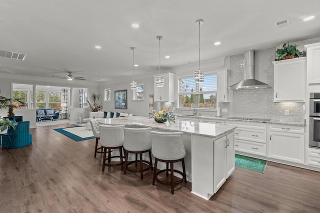 kitchen featuring wall chimney range hood, a center island, white cabinetry, decorative backsplash, and visible vents