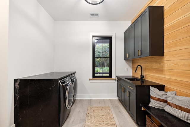 laundry room featuring washing machine and clothes dryer, light hardwood / wood-style floors, cabinets, and sink