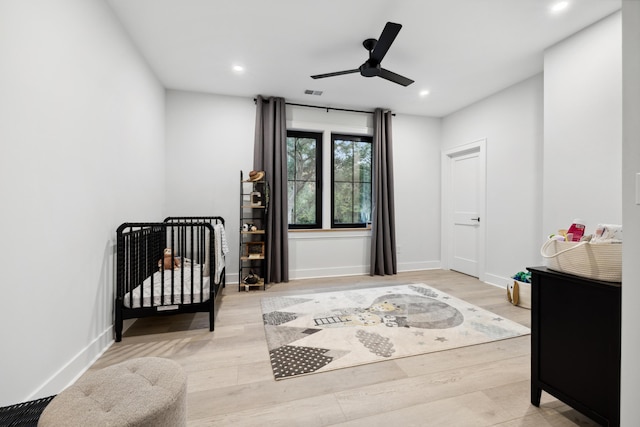 bedroom with light hardwood / wood-style floors, ceiling fan, and a nursery area