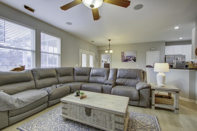 living room with ceiling fan with notable chandelier and light wood-type flooring