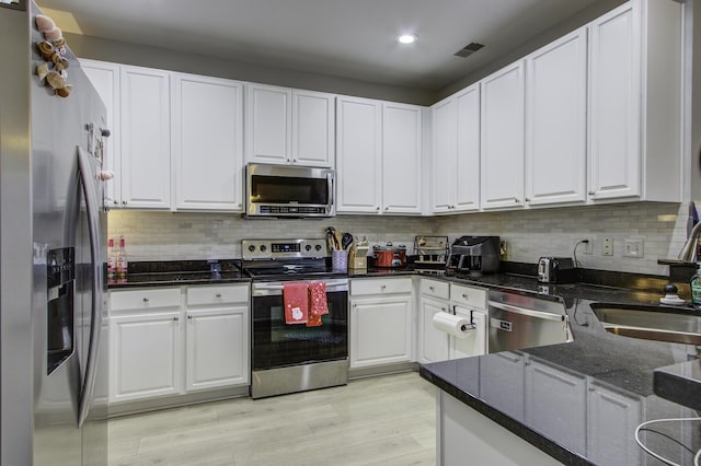 kitchen with white cabinetry, sink, stainless steel appliances, light hardwood / wood-style flooring, and dark stone countertops