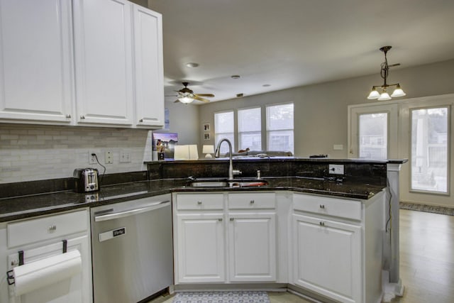 kitchen with kitchen peninsula, white cabinets, sink, dark stone countertops, and dishwasher