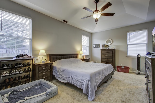 bedroom with a raised ceiling, ceiling fan, and light carpet