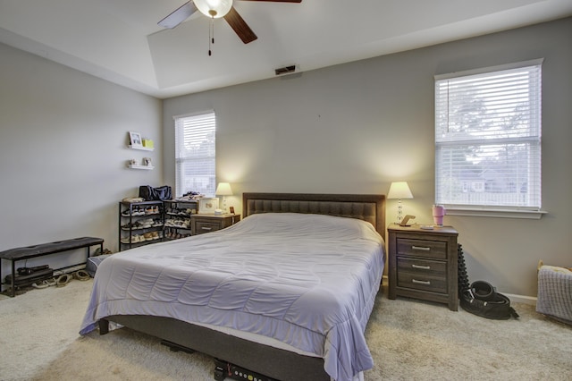 bedroom with light colored carpet, a raised ceiling, and ceiling fan