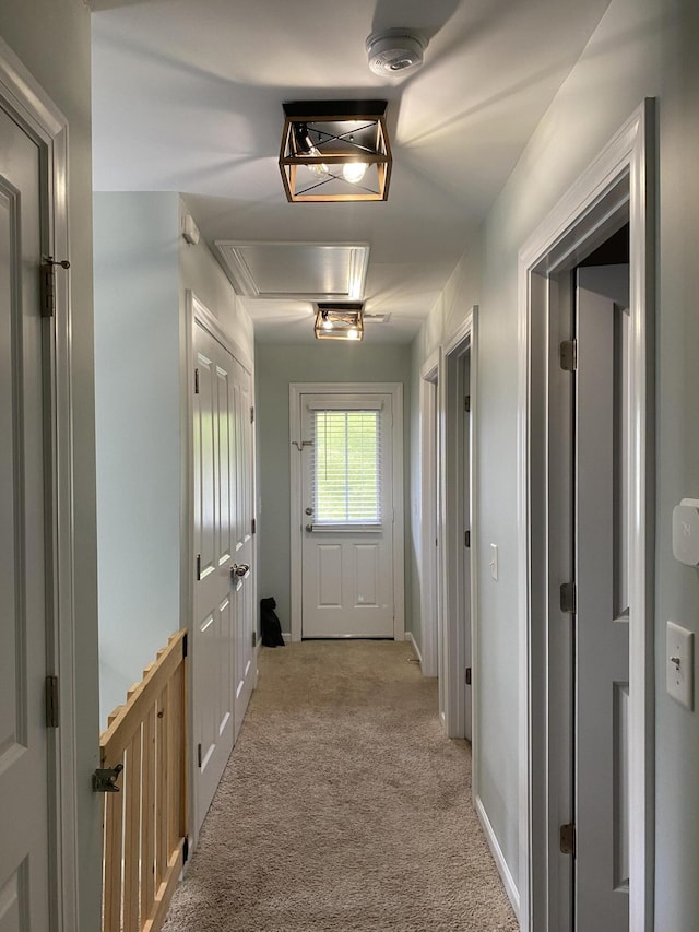 hallway with attic access, light colored carpet, and baseboards