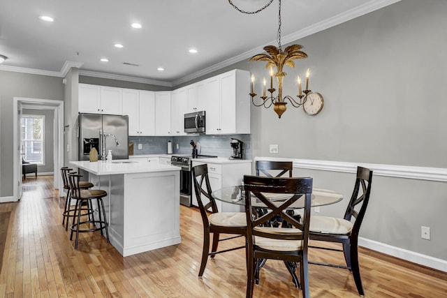 kitchen with appliances with stainless steel finishes, white cabinetry, hanging light fixtures, and ornamental molding