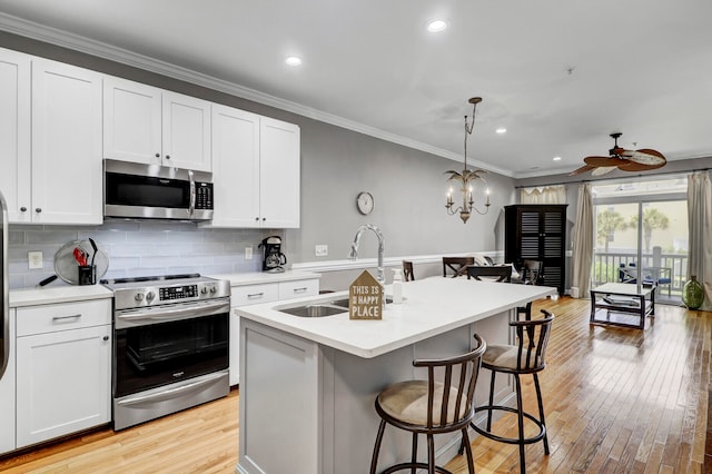 kitchen featuring a kitchen island with sink, ceiling fan with notable chandelier, appliances with stainless steel finishes, white cabinetry, and a breakfast bar area