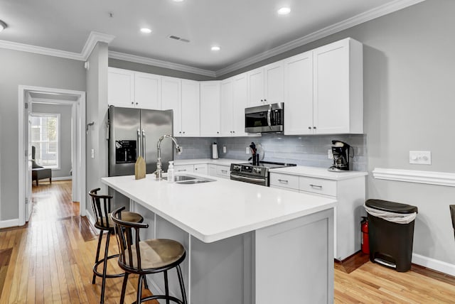 kitchen with sink, a breakfast bar area, an island with sink, white cabinetry, and stainless steel appliances