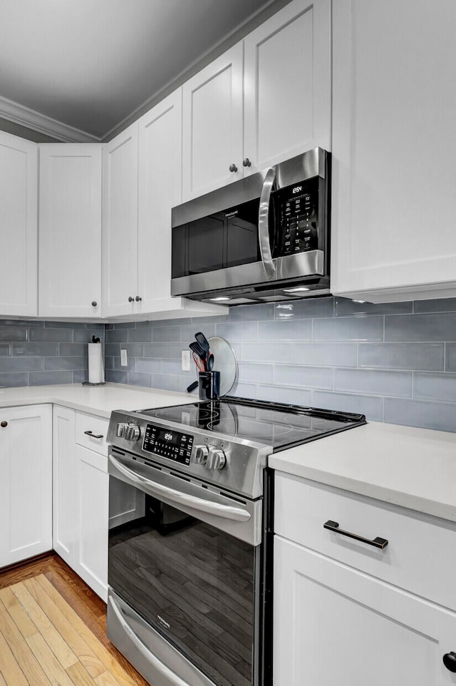 kitchen featuring white cabinets, light wood-type flooring, stainless steel appliances, and backsplash