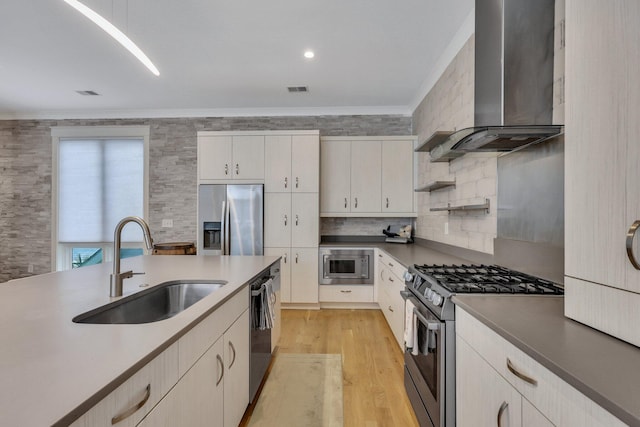 kitchen featuring sink, wall chimney exhaust hood, stainless steel appliances, light hardwood / wood-style flooring, and crown molding