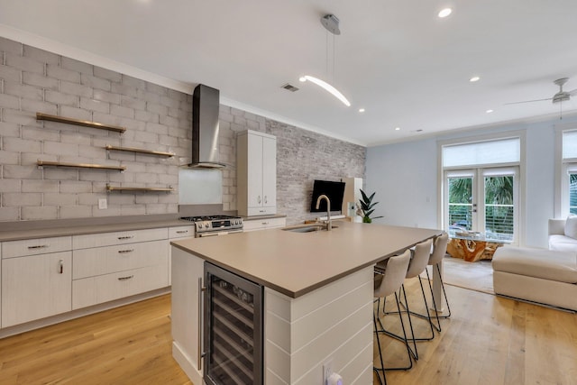 kitchen with wall chimney exhaust hood, sink, white cabinets, light hardwood / wood-style floors, and wine cooler