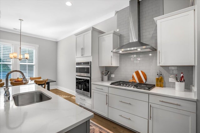 kitchen featuring wall chimney range hood, white cabinets, ornamental molding, stainless steel appliances, and sink