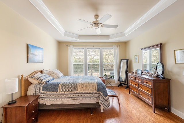 bedroom featuring ceiling fan, ornamental molding, a tray ceiling, and light wood-type flooring