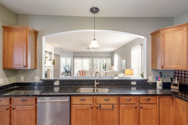 kitchen featuring sink, hanging light fixtures, stainless steel dishwasher, ceiling fan, and dark stone counters