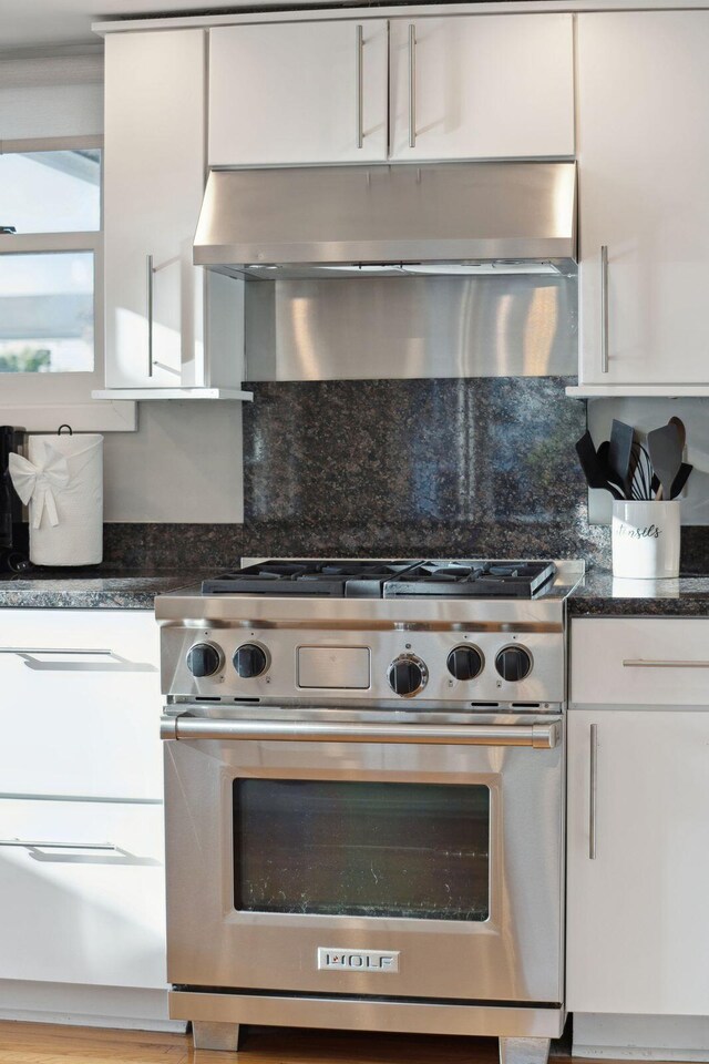 kitchen featuring white cabinetry, stainless steel range, and dark stone counters