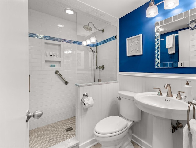 bathroom with tiled shower, toilet, wooden walls, and sink