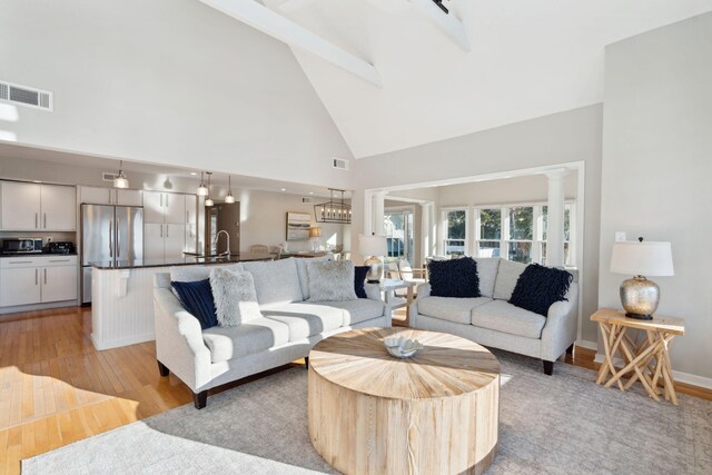 living room featuring sink, light hardwood / wood-style flooring, high vaulted ceiling, beamed ceiling, and decorative columns