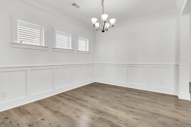 empty room featuring hardwood / wood-style floors, ornamental molding, and a chandelier