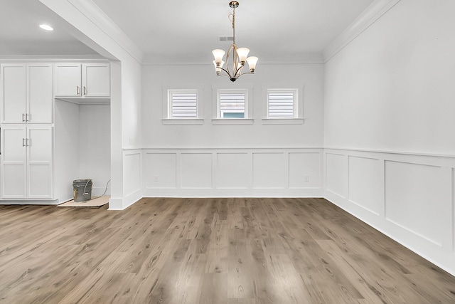 unfurnished dining area featuring light wood-type flooring, crown molding, and an inviting chandelier