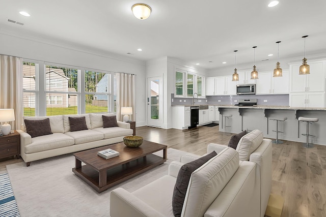 living room with ornamental molding, sink, and light hardwood / wood-style floors