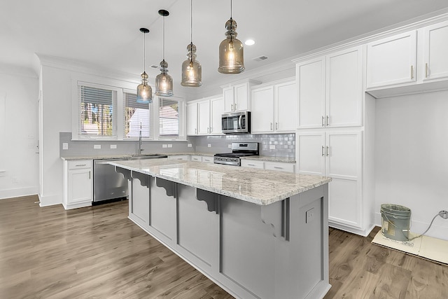 kitchen with dark hardwood / wood-style flooring, decorative light fixtures, white cabinets, appliances with stainless steel finishes, and a center island