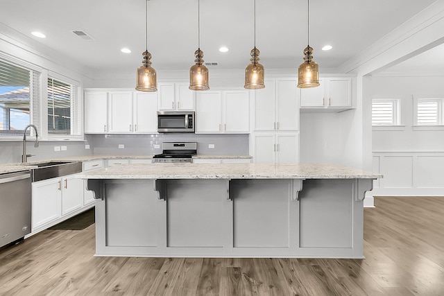 kitchen featuring light stone countertops, appliances with stainless steel finishes, hanging light fixtures, and a center island