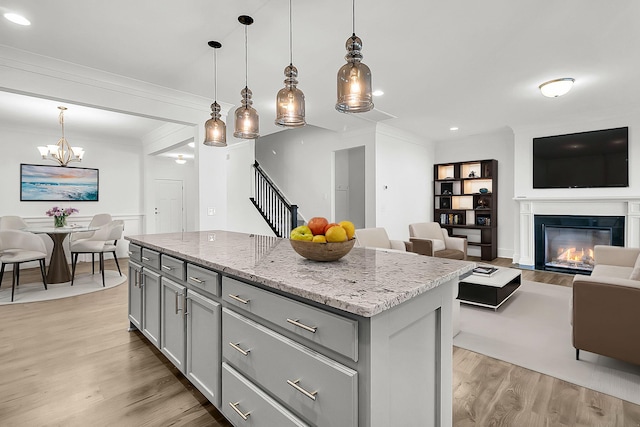 kitchen with light stone counters, a center island, gray cabinetry, pendant lighting, and light hardwood / wood-style flooring