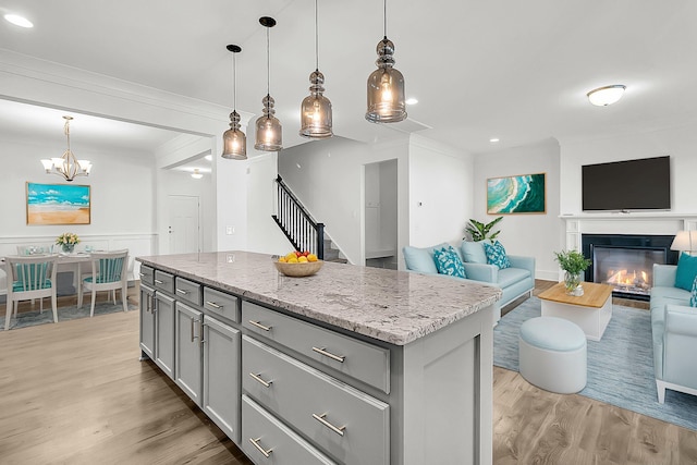 kitchen featuring gray cabinetry, light wood-type flooring, a kitchen island, decorative light fixtures, and light stone countertops