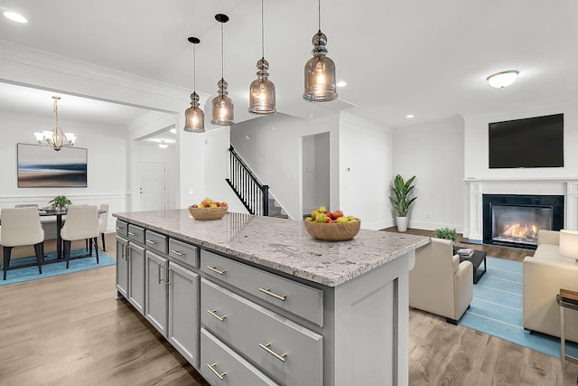 kitchen with light stone countertops, a center island, gray cabinetry, light hardwood / wood-style floors, and hanging light fixtures