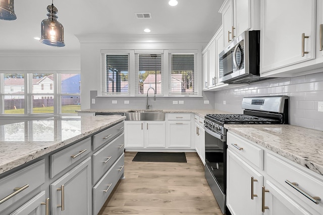 kitchen with light wood-type flooring, sink, pendant lighting, white cabinetry, and appliances with stainless steel finishes