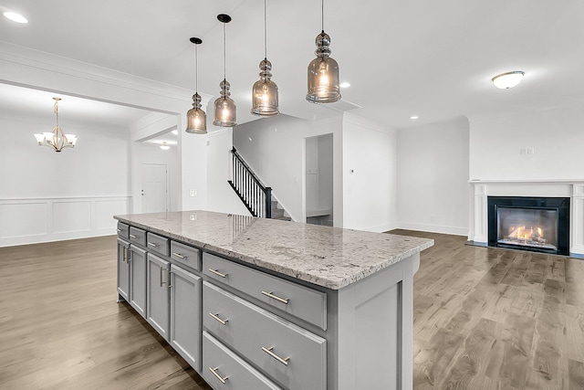 kitchen featuring gray cabinetry, hardwood / wood-style floors, a kitchen island, light stone counters, and hanging light fixtures