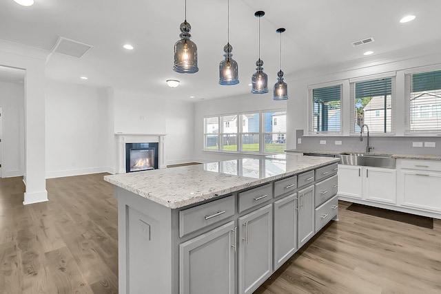 kitchen with pendant lighting, ornamental molding, sink, a kitchen island, and wood-type flooring