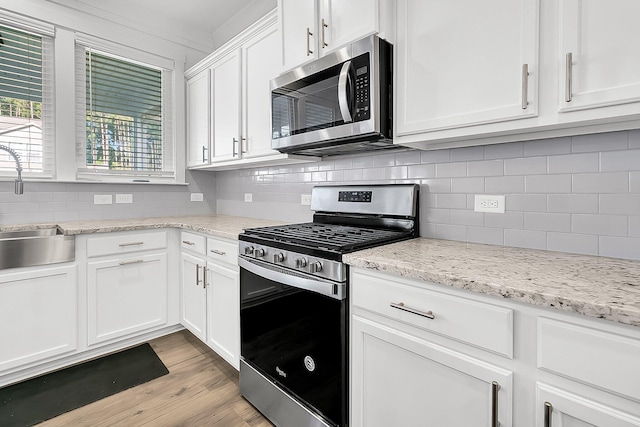 kitchen with light stone counters, stainless steel appliances, sink, light hardwood / wood-style floors, and white cabinetry