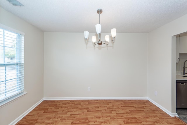 unfurnished dining area featuring a notable chandelier, plenty of natural light, a textured ceiling, and light wood-type flooring