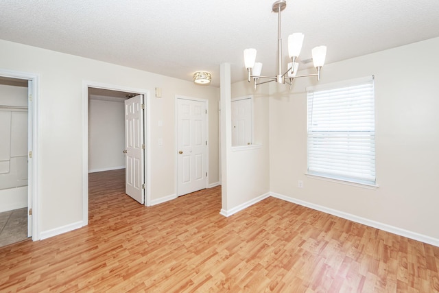 unfurnished dining area featuring an inviting chandelier, a textured ceiling, and light wood-type flooring