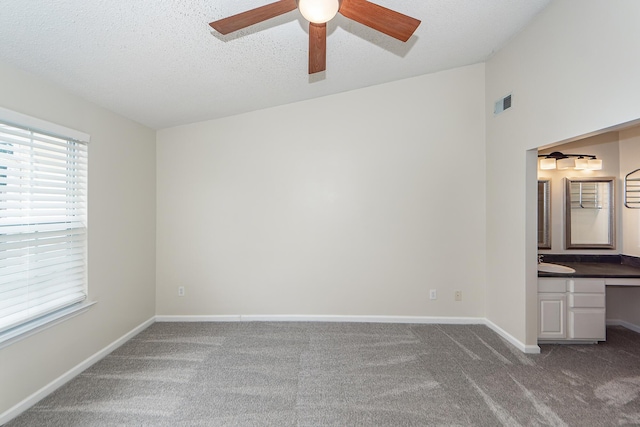 interior space featuring ceiling fan, sink, dark carpet, and a textured ceiling