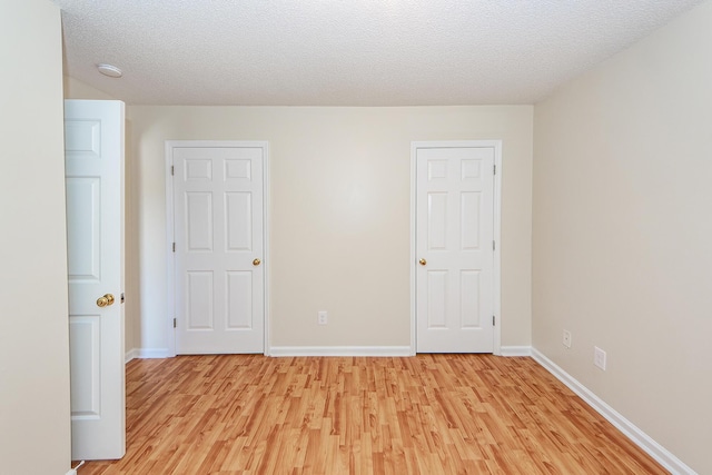 empty room with a textured ceiling and light hardwood / wood-style flooring