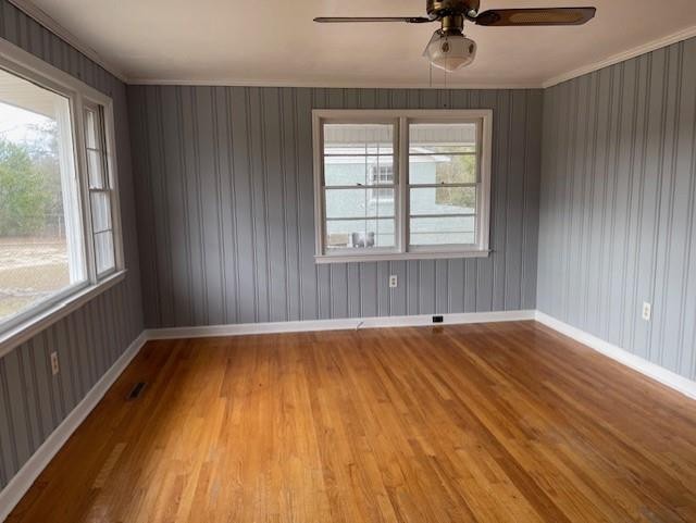 empty room with light hardwood / wood-style floors, ornamental molding, a wealth of natural light, and ceiling fan