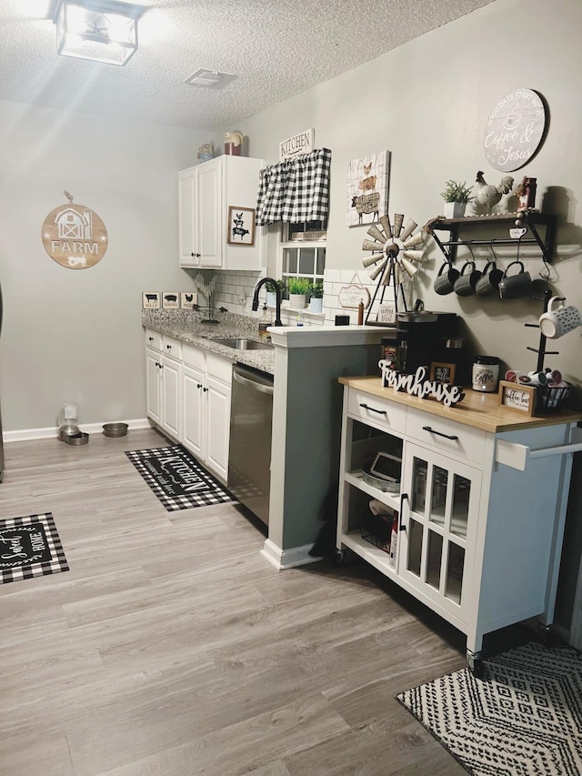 kitchen featuring sink, light hardwood / wood-style flooring, white cabinetry, a textured ceiling, and stainless steel dishwasher