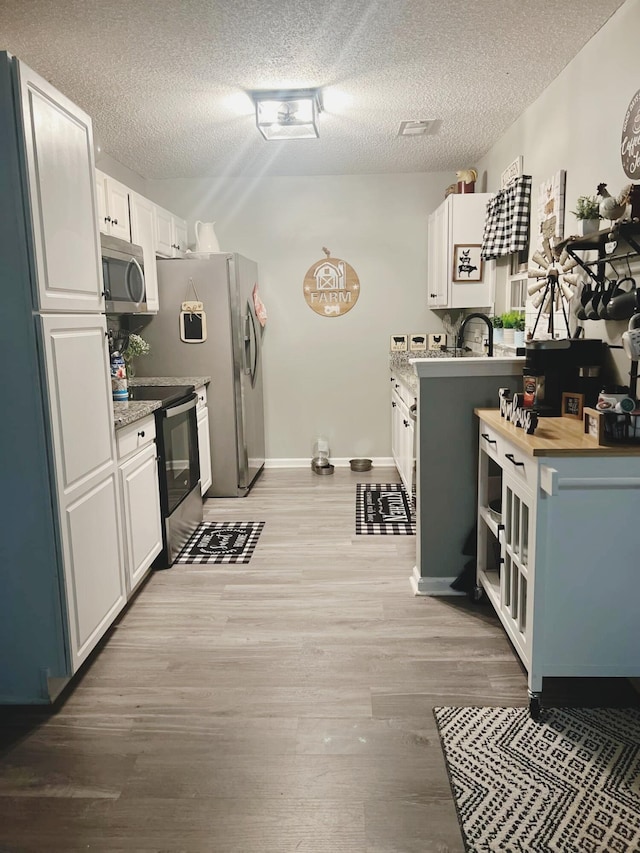 kitchen featuring stainless steel appliances, a textured ceiling, white cabinets, and light hardwood / wood-style floors