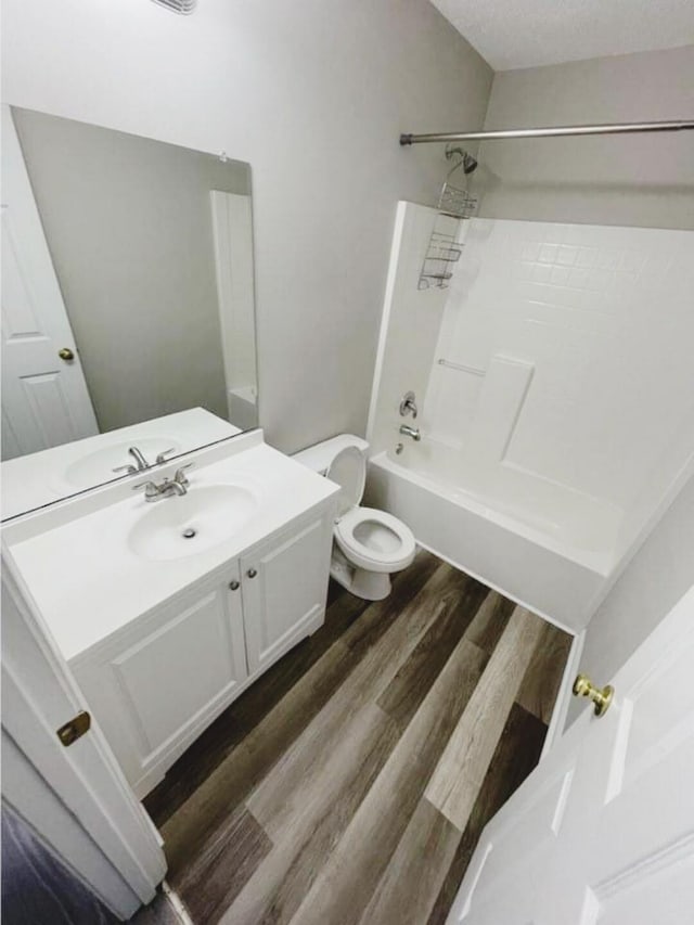 full bathroom with hardwood / wood-style floors, shower / bathing tub combination, vanity, toilet, and a textured ceiling