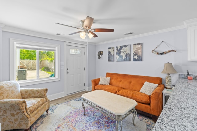 living area featuring light wood-style flooring, baseboards, visible vents, ceiling fan, and ornamental molding