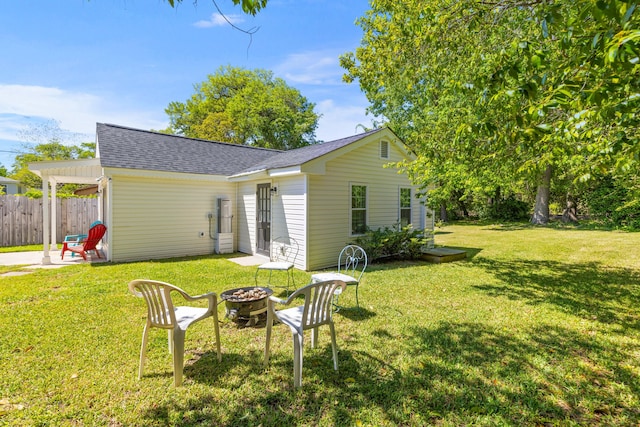 back of house featuring a lawn, fence, roof with shingles, and an outdoor fire pit