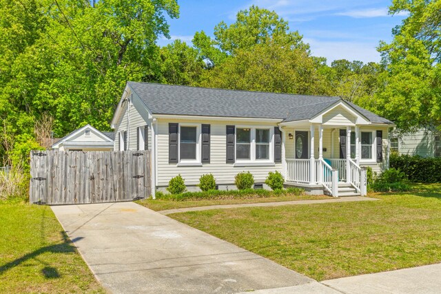 view of front facade with a gate, a shingled roof, driveway, covered porch, and a front yard