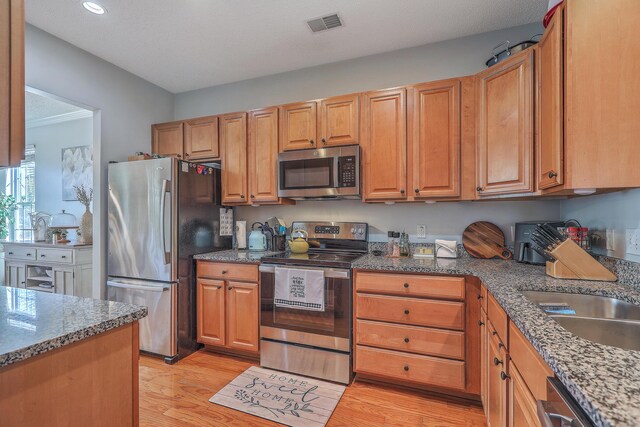 kitchen with stone counters, light wood-style flooring, visible vents, and appliances with stainless steel finishes