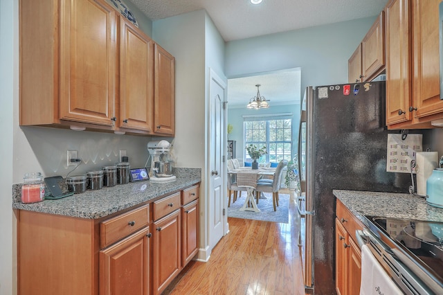 kitchen with a chandelier, a textured ceiling, light wood-type flooring, and light stone countertops