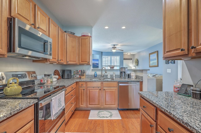 kitchen featuring a ceiling fan, stone counters, a peninsula, a sink, and appliances with stainless steel finishes