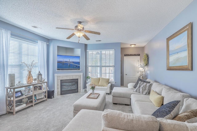 carpeted living area with a healthy amount of sunlight, a fireplace, a textured ceiling, and ceiling fan