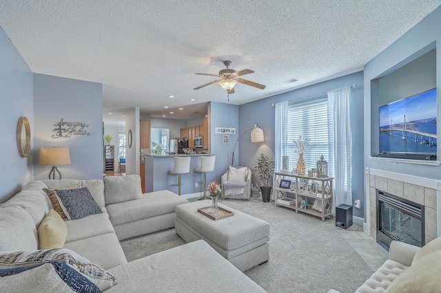 living area with visible vents, a tiled fireplace, a textured ceiling, baseboards, and ceiling fan